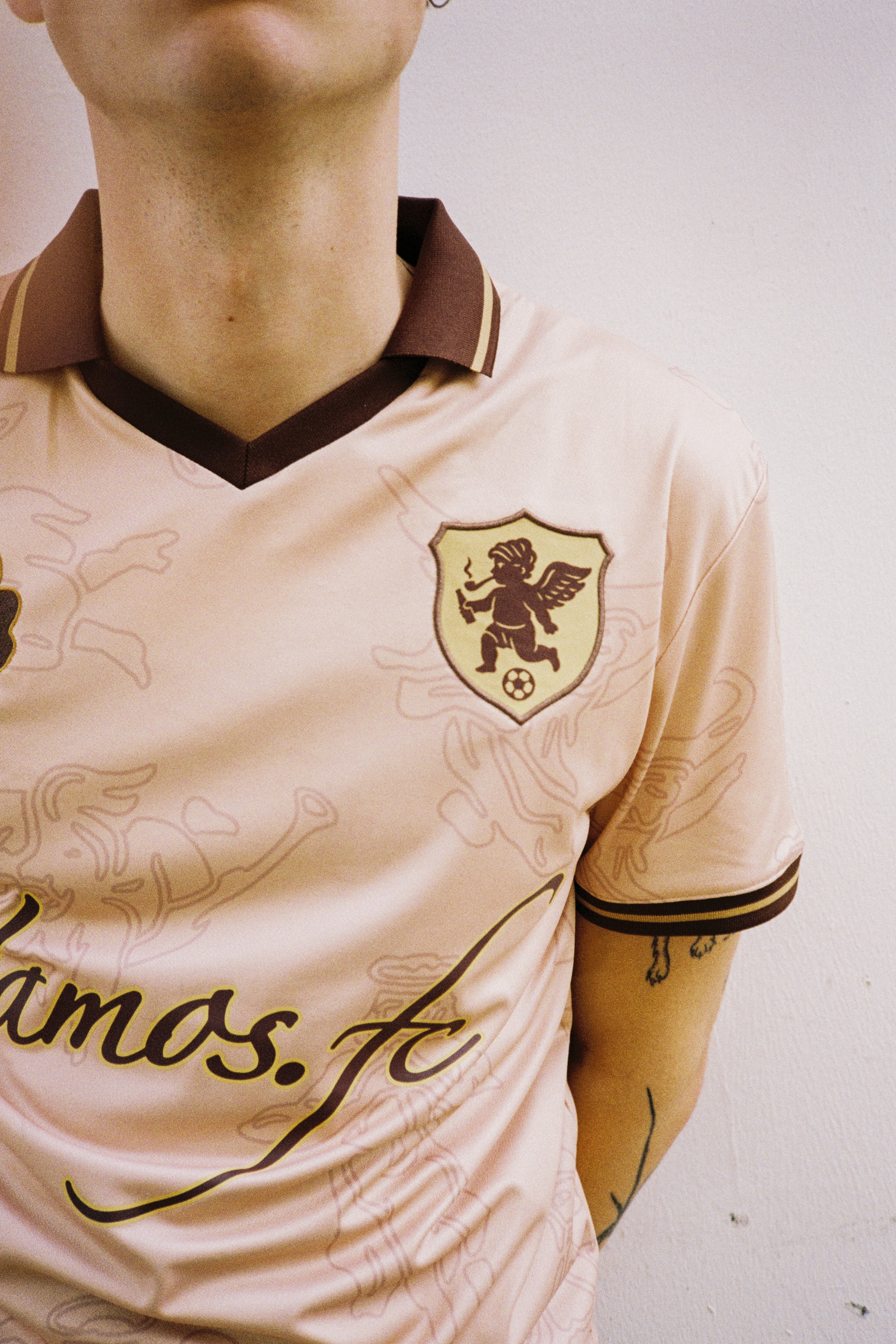 Close-up of the andvamos Footy Shirt — embroidered VAMOS FC cherub crest on cream limited-edition streetwear jersey